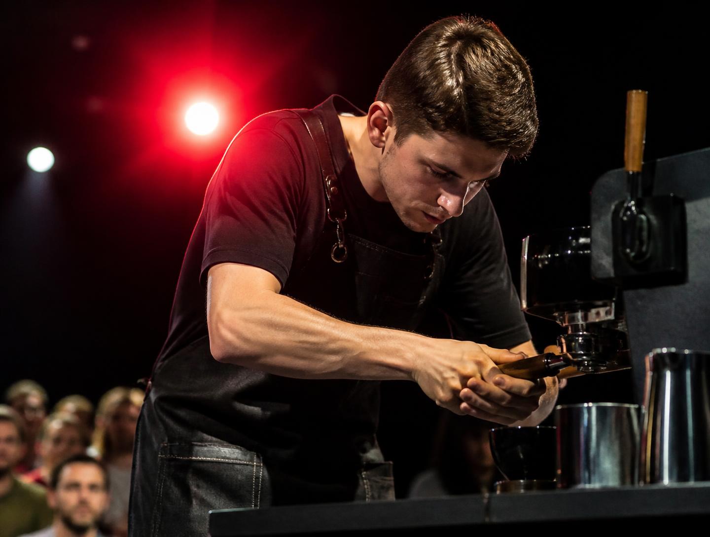 Barista competing under stage lighting, hands on the group head